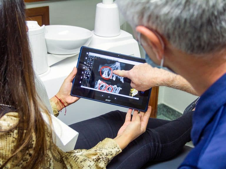 Wisdom Teeth Removal - Over the shoulder image of a dentist pointing to an Xray on a tablet, talking to a patient.